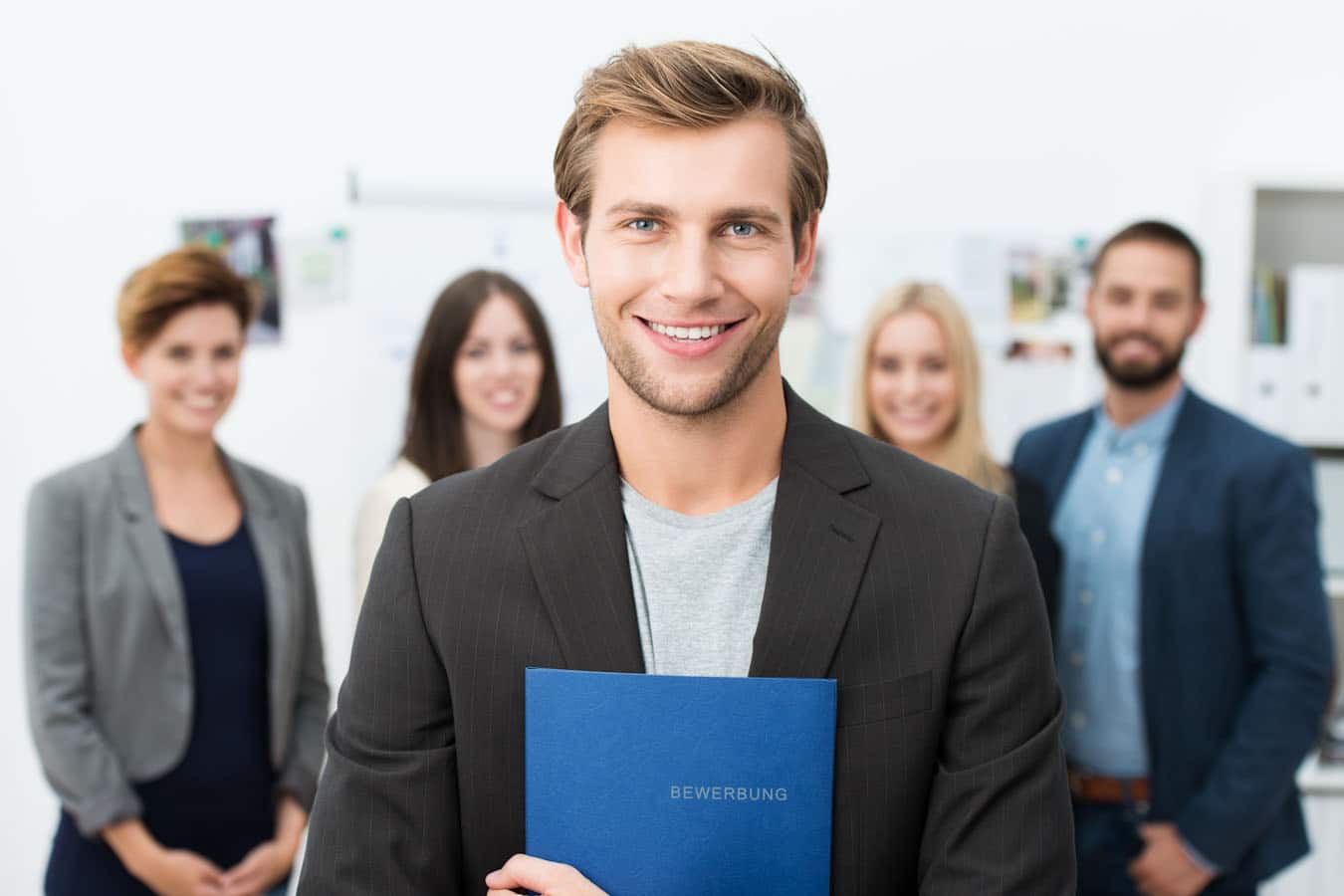 Молодой человек с резюме в голубой папке на фоне коллег